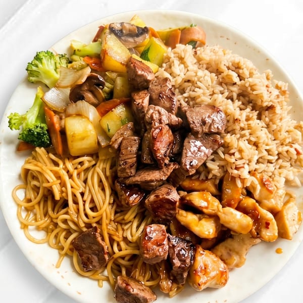 A plate of hibachi-style food with steak, chicken, noodles, rice, and mixed vegetables.