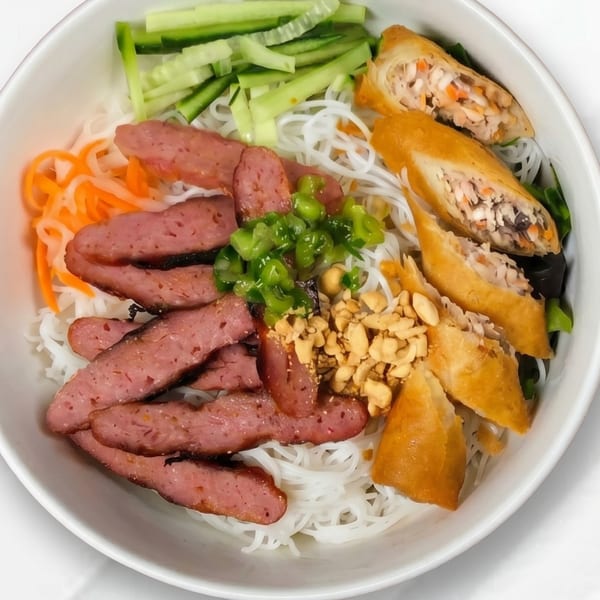 Vietnamese vermicelli noodle bowl with grilled pork sausage, crispy spring rolls, and fresh vegetables.